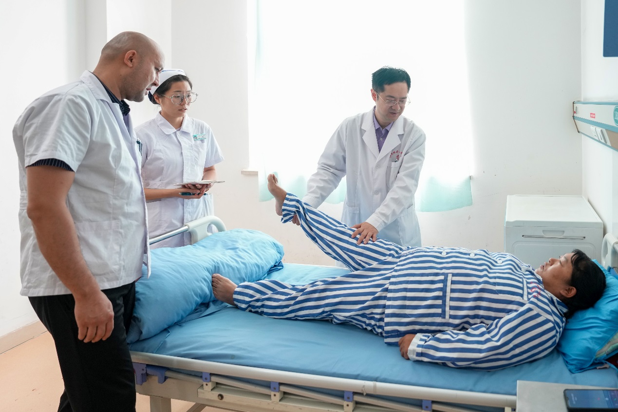 在和田地區人民醫院掛職骨科副主任的北京積水潭醫院脊柱外科副主任醫師於傑（右一），在進行教學查房，講解腰椎間盤突出症患者體格檢查要點，並為該患者即將進行的腰椎微創手術進行方案設計和術前準備。
